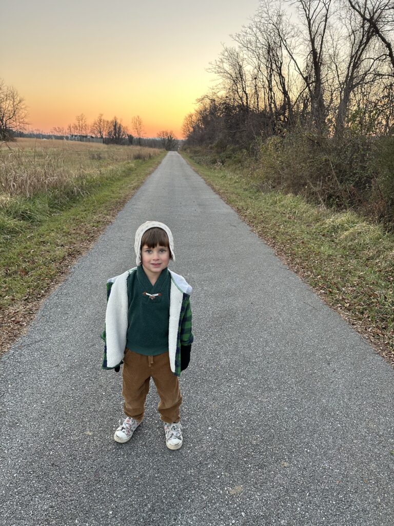 Boy standing on trail in front of sunset
